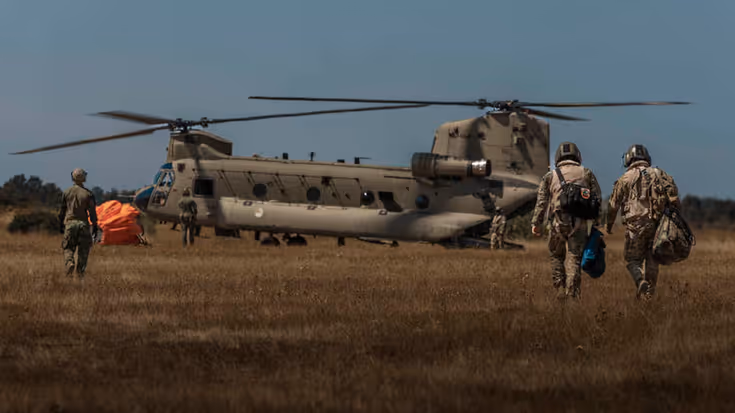 4 militairen op de rug gezien lopen naar een Chinook-transporthelikopter.