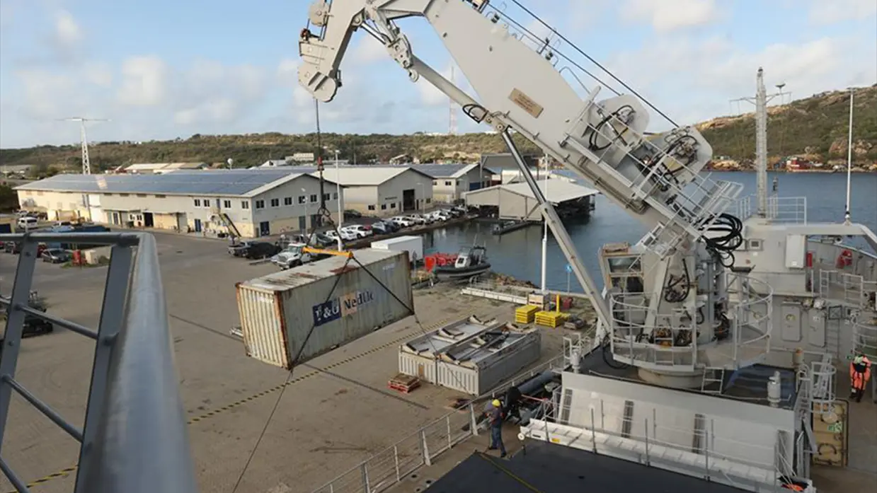 Een container hangt in de kraan van Zr.Ms. Pelikaan boven een kade