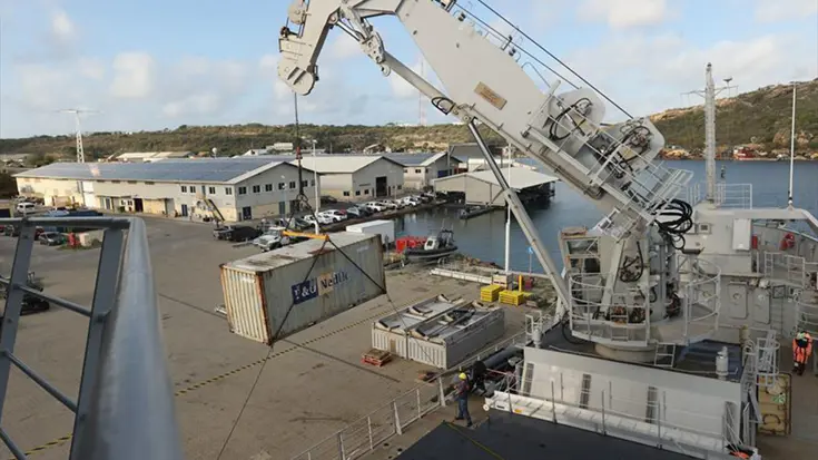 Een container hangt in de kraan van Zr.Ms. Pelikaan boven een kade