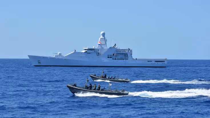 Een marineschip op zee, geflankeerd door snelle onderscheppingsboten.