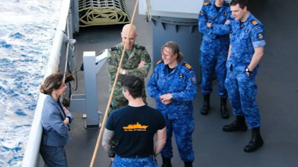 De minister praat met militairen aan boord van een schip.