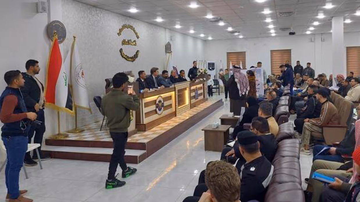 De minister spreekt een zaal toe in Irak.