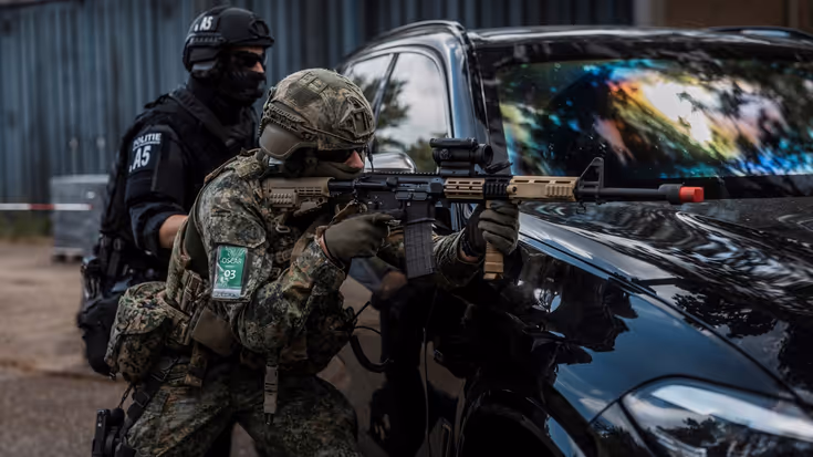 Agent en militair bukken naast een auto.