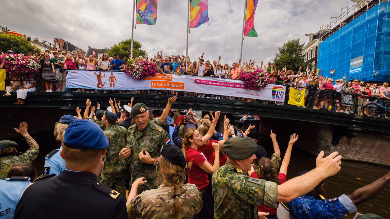 Militairen wuiven vanaf de gracht naar het publiek op een brug.