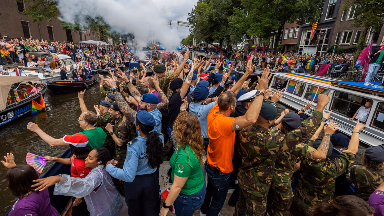 Militairen en burgers wuiven mensen toe vanaf de gracht.