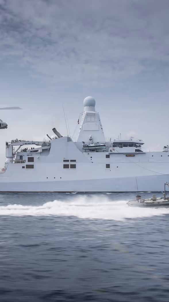 Schip op zee met boot die er naast vaart en een helikopter volgt.