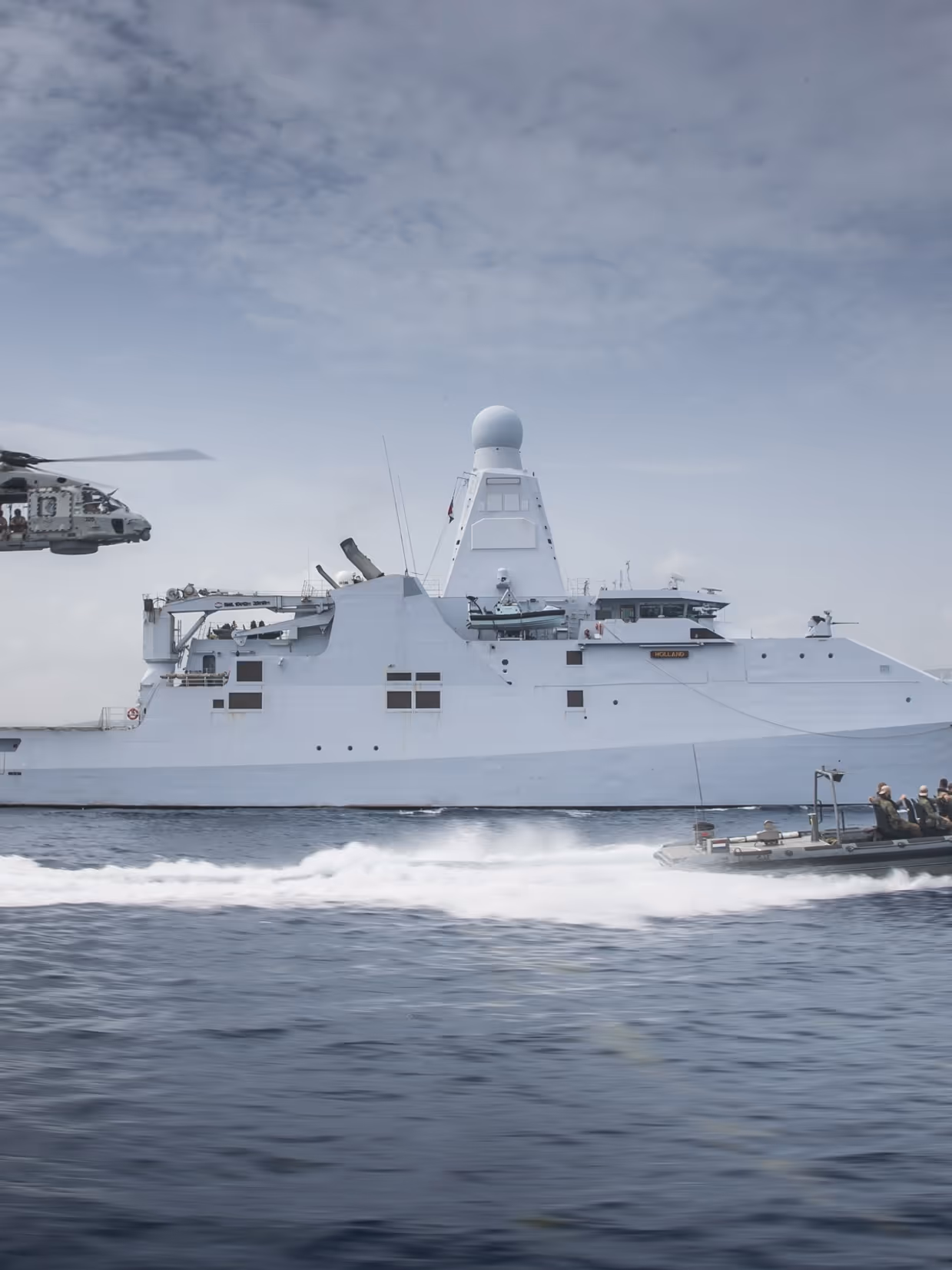 Schip op zee met boot die er naast vaart en een helikopter volgt.