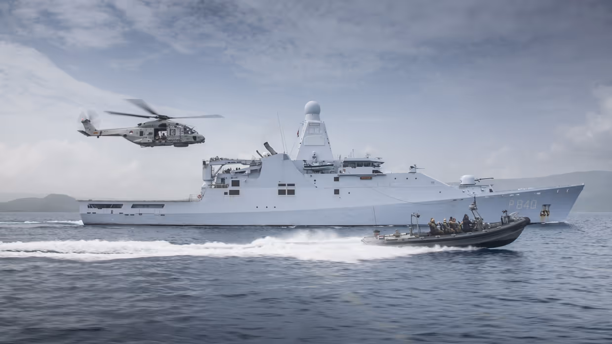Schip op zee met boot die er naast vaart en een helikopter volgt.