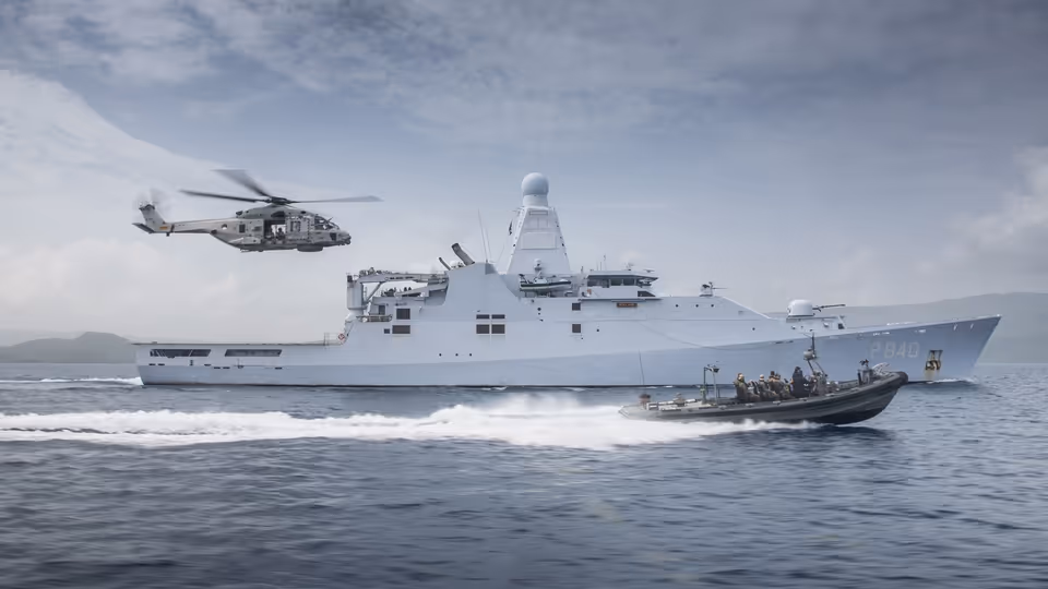 Schip op zee met boot die er naast vaart en een helikopter volgt.
