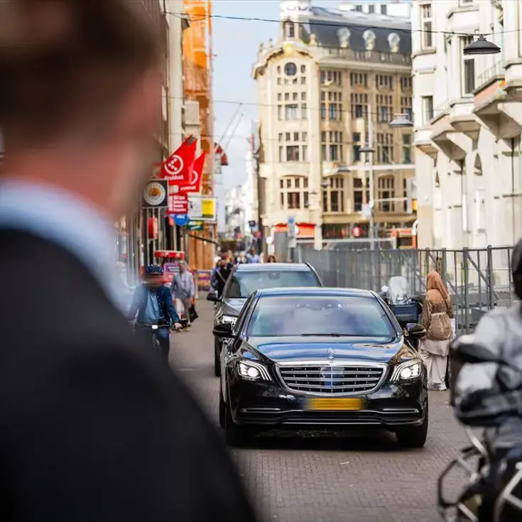 Een beveiliger op de voorgrond kijkt naar aankomende auto’s in de binnenstad.