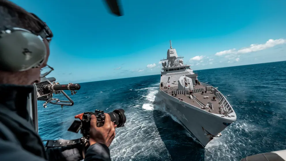 Een marinier kijkt vanaf zijn schip naar zijn camera. Voor hem ligt een ander schip.