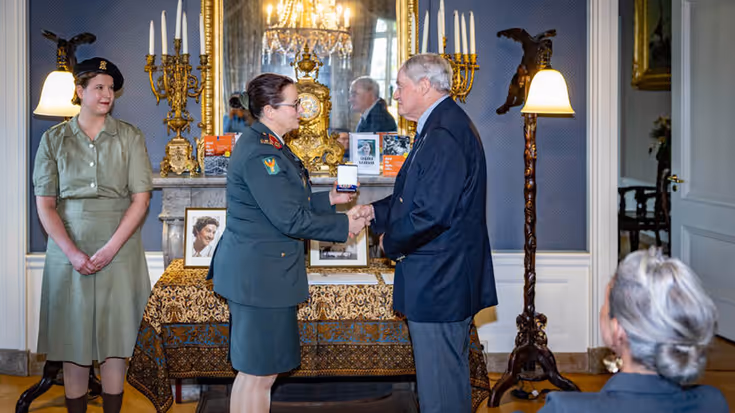 Militair overhandigt nabestaande onderscheiding.