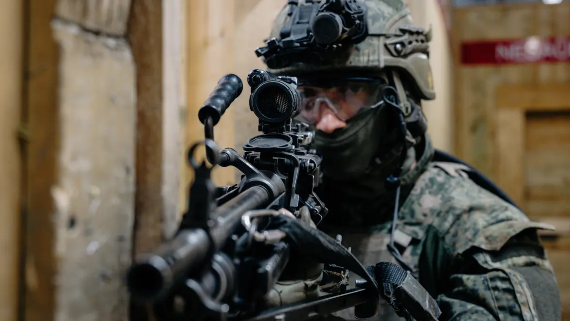 Een militair met een groot geweer en een helm op. 