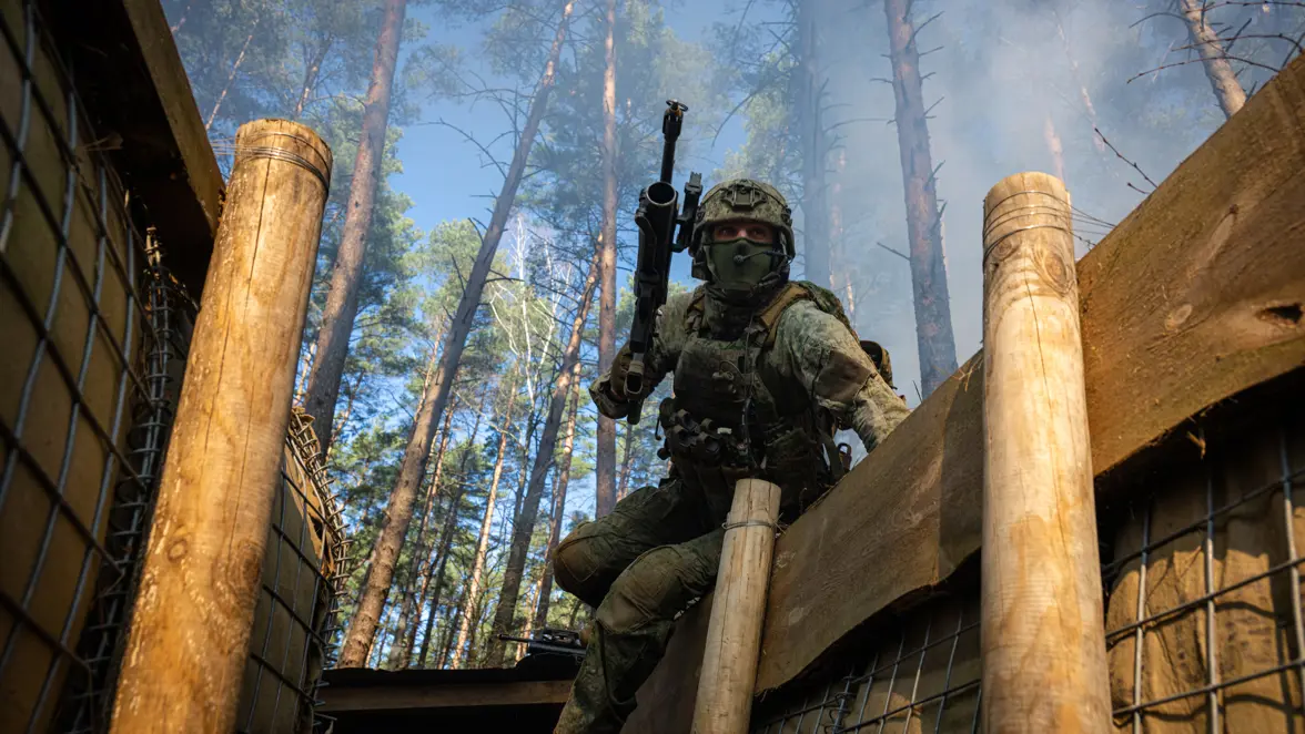 Militairen in loopgraven met geweren en helmen op.
