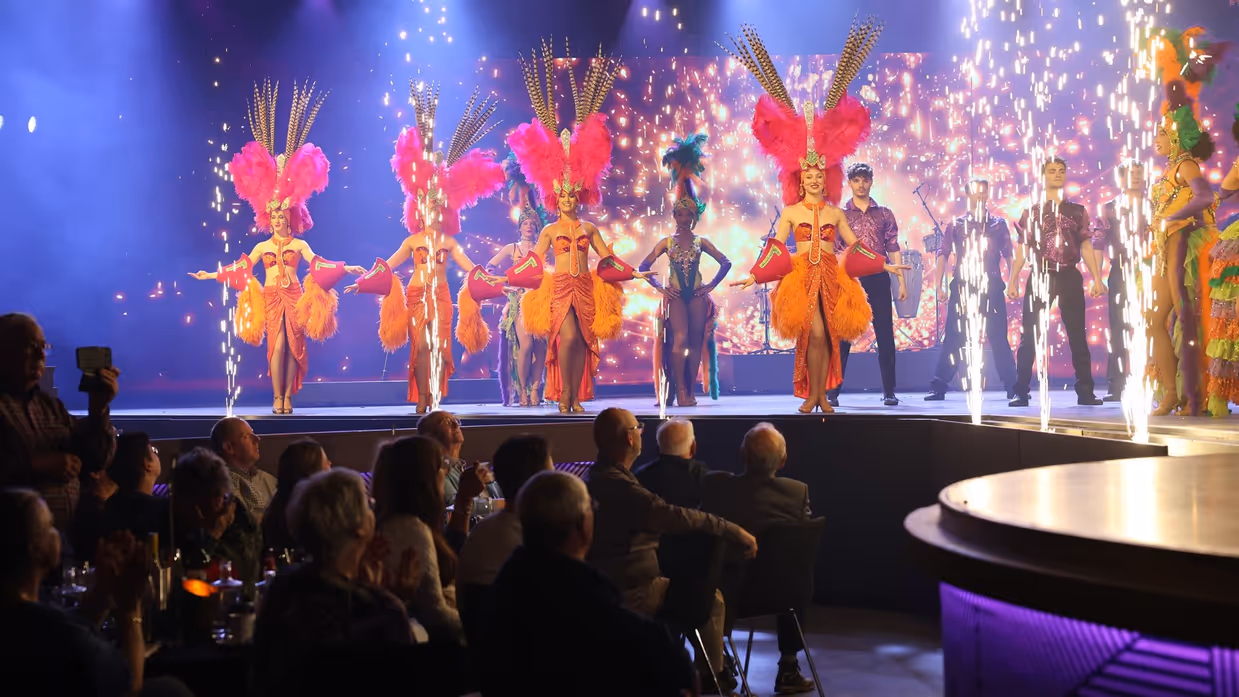 Danseressen, dansers en vuurwerk op een podium voor publiek.