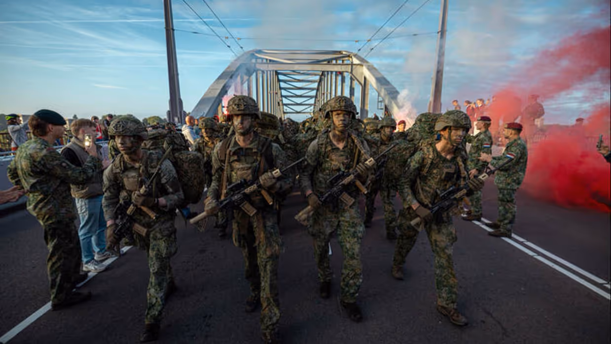 Militairen in volle bepakking marcheren over brug.