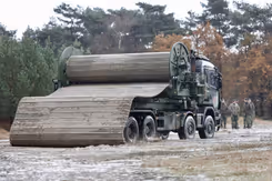 Wegenmattenlegger staat geparkeerd aan rand van bos.