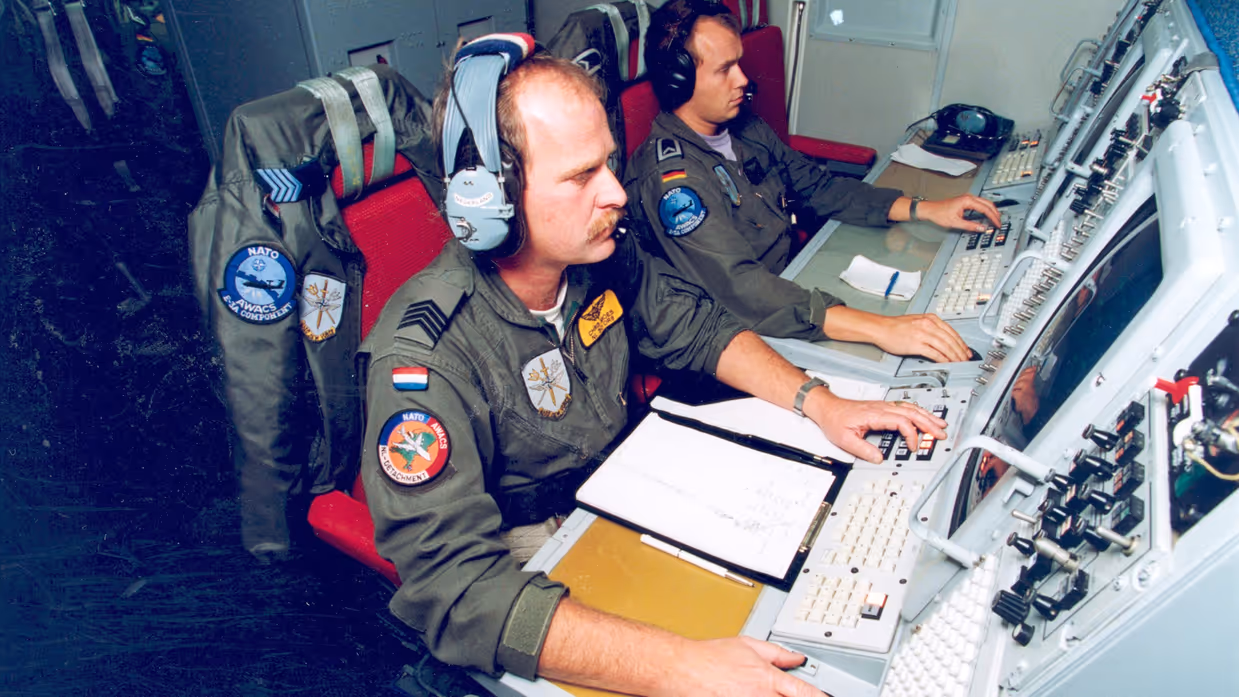  Twee militairen achter radarschermen in een vliegtuig.