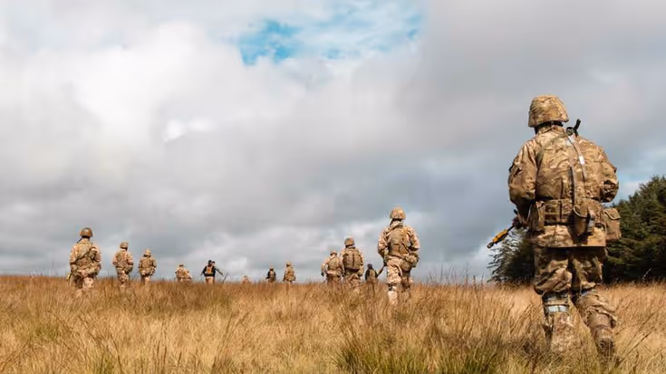 Militairen lopen door graslandschap.