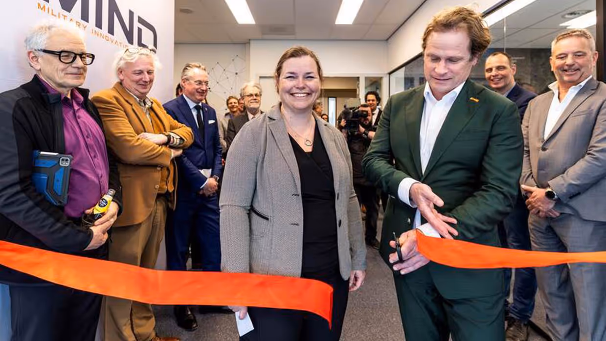Gijs Tuinman knipt oranje lint door.  Een vrouw naast hem. Mensen langs de zijlijn.