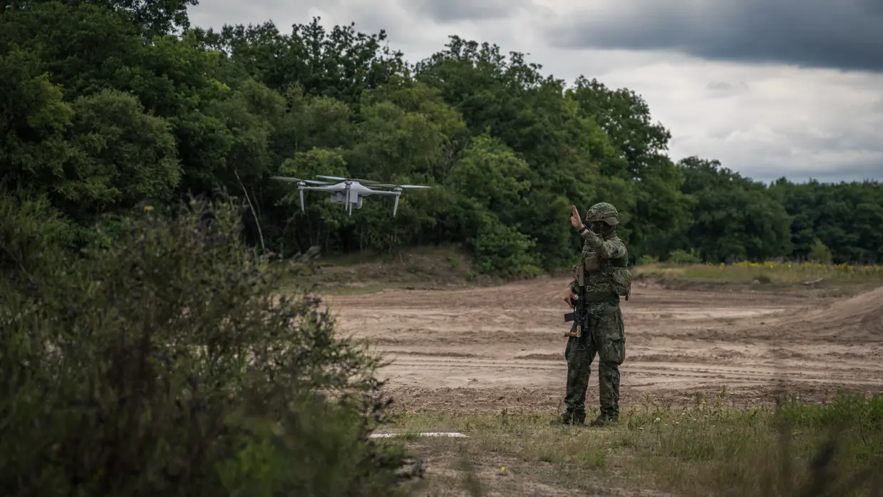 Een militair kijkt naar een drone die landt. 