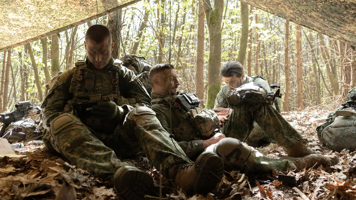 Militairen rusten en bereiden zich voor onder een gecamoufleerd schuilzeil.