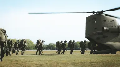Militairen met zware bepakking lopen richting een Chinook-helikopter.