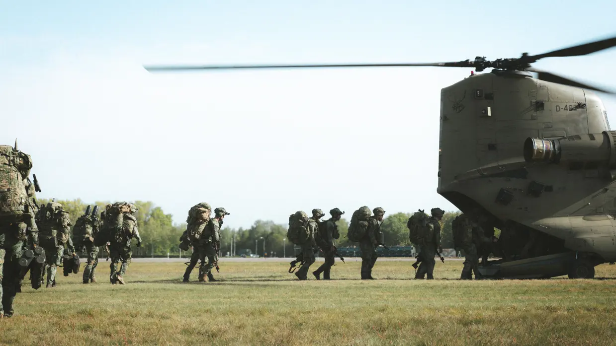 Militairen met zware bepakking lopen richting een Chinook-helikopter.