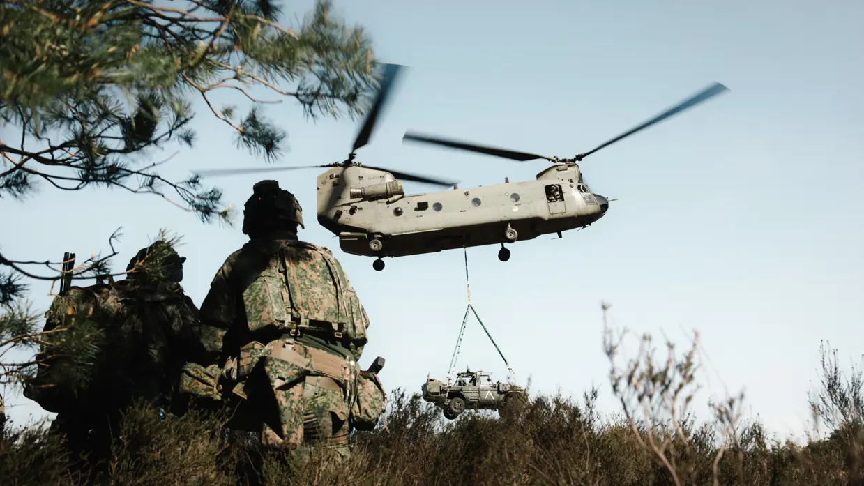 Militairen met zware bepakking lopen richting een Chinook-helikopter.