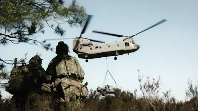 Militairen met zware bepakking lopen richting een Chinook-helikopter.