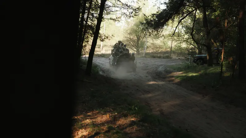 Militairen verplaatsen zich met een voertuig over een zandpad door het bos tijdens oefening Versatile Guard.