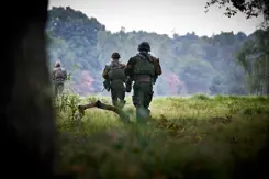 Militairen van achteren gezien lopen door een landschap.
