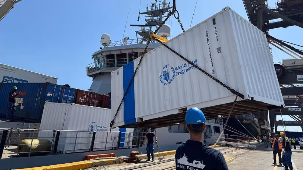Een witte container met World Food Programme in blauw erop wordt aan land gezet.