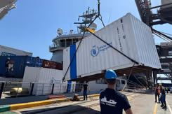 Een witte container met World Food Programme in blauw erop wordt aan land gezet.