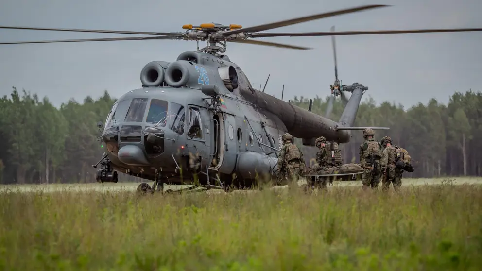 Militairen brengen een militair op een brancard naar een helikopter.