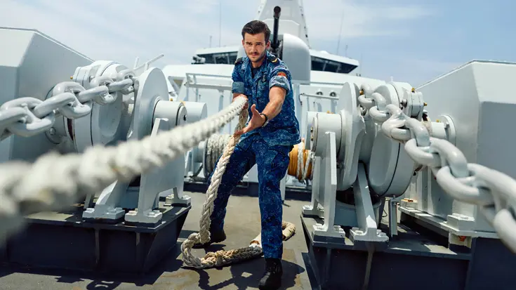 Een marineman hangt aan een kabel op het voordek van een marineschip.